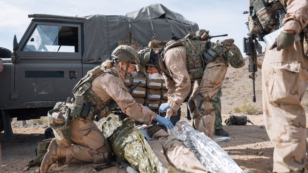 Militairen helpen een gewonde collega die op de grond ligt. 