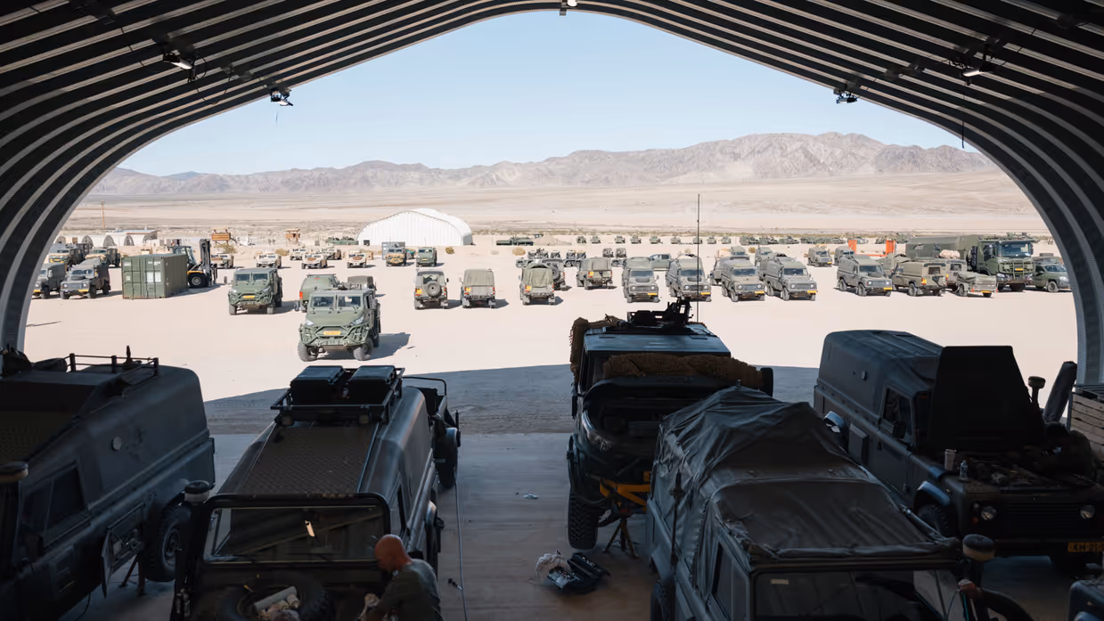 Een grote groep voertuigen staat in de woestijn, deels overkapt. 