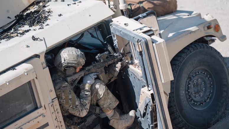 Een militair richt zijn wapen vanuit de openstaande deur van een voertuig. 