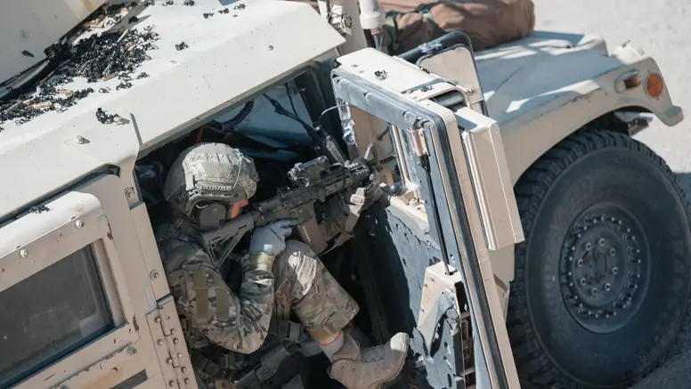Een militair richt zijn wapen vanuit de openstaande deur van een voertuig. 