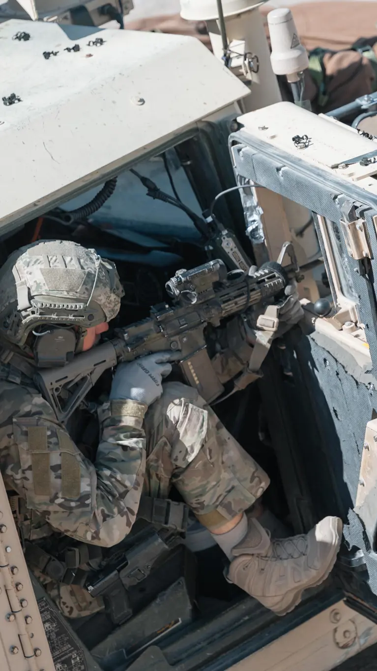 Een militair richt zijn wapen vanuit de openstaande deur van een voertuig. 