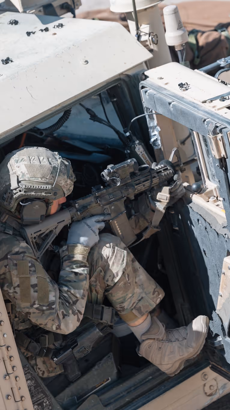 Een militair richt zijn wapen vanuit de openstaande deur van een voertuig. 