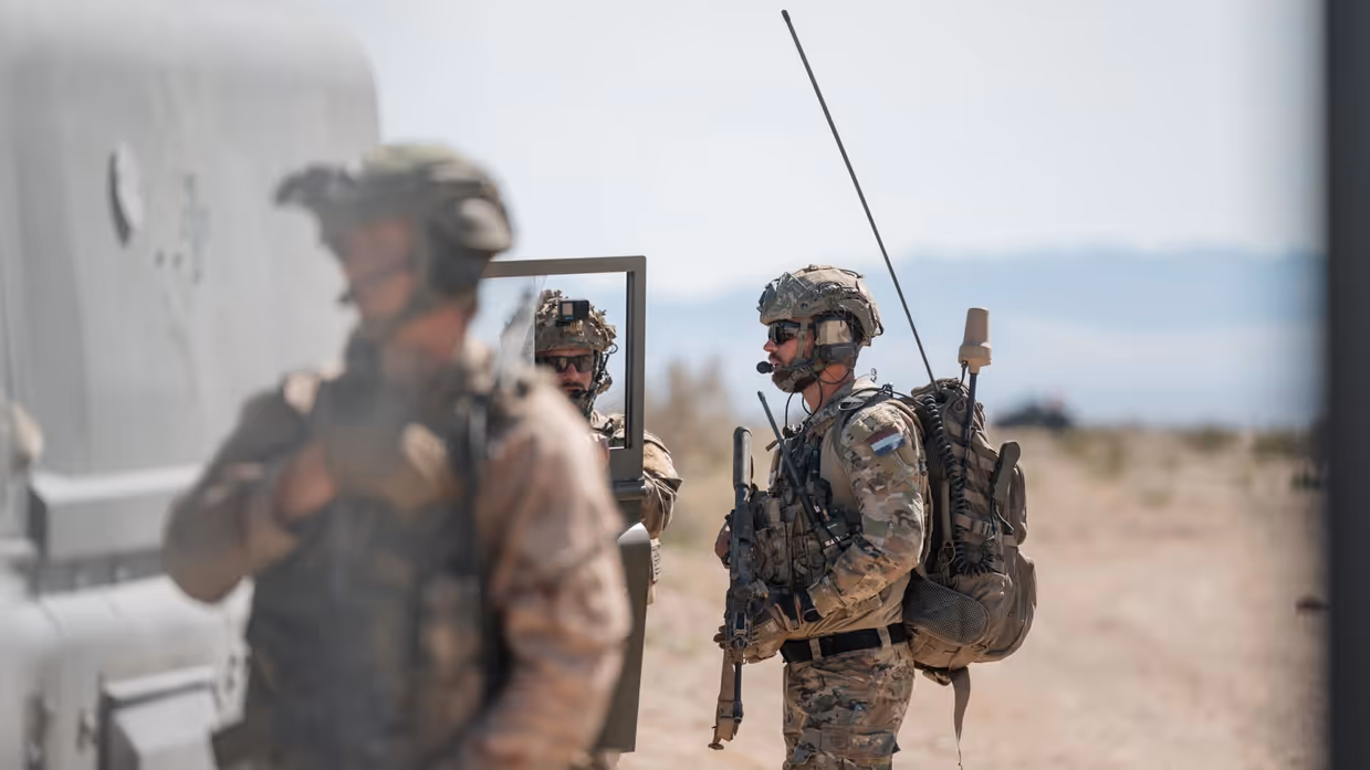 Drie militairen in de woestijn staan bij een voertuig.