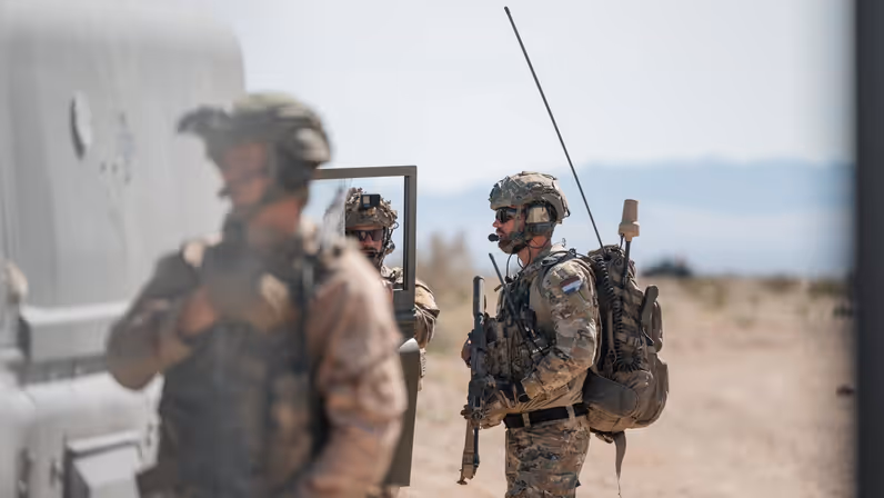 Drie militairen in de woestijn staan bij een voertuig.