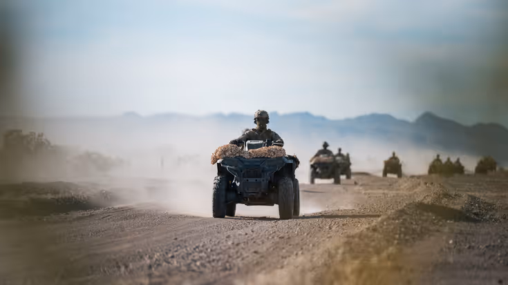 Een militair komt door de woestijn aanrijden op een quad. 