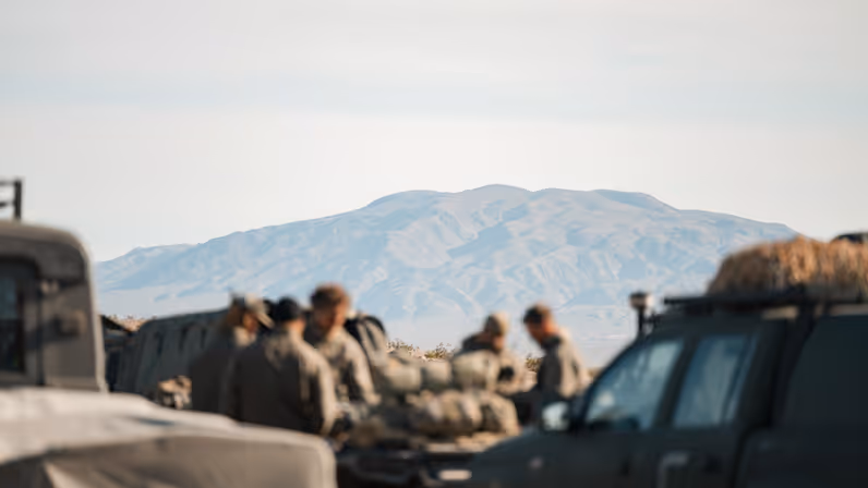 Een groep militairen met op de achtergrond een berg in de Mojave-woestijn. 