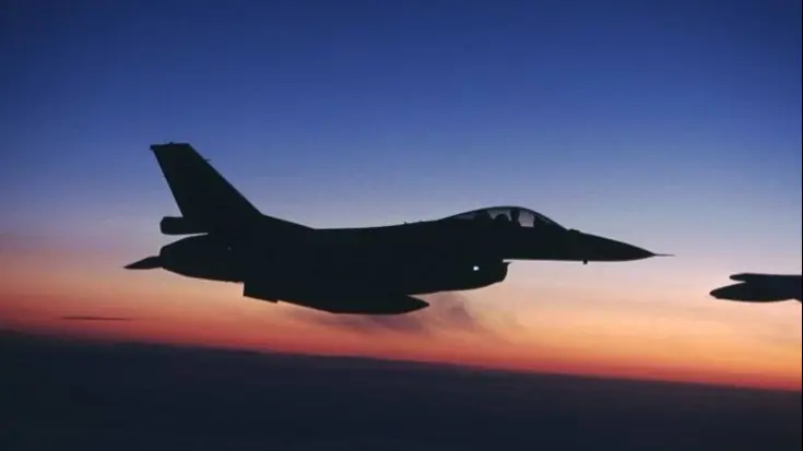 Een F-16 vliegt bij schemering in blauw-oranje lucht.
