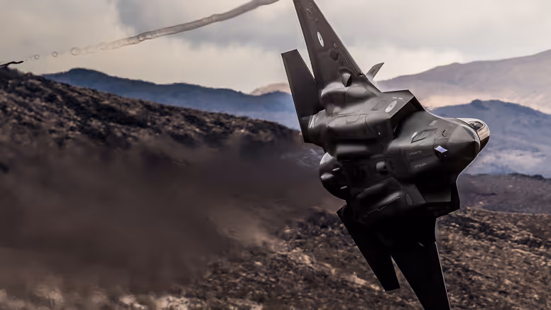Een F-35 scheert door de lucht, op de achtergrond zijn bruine bergen te zien 