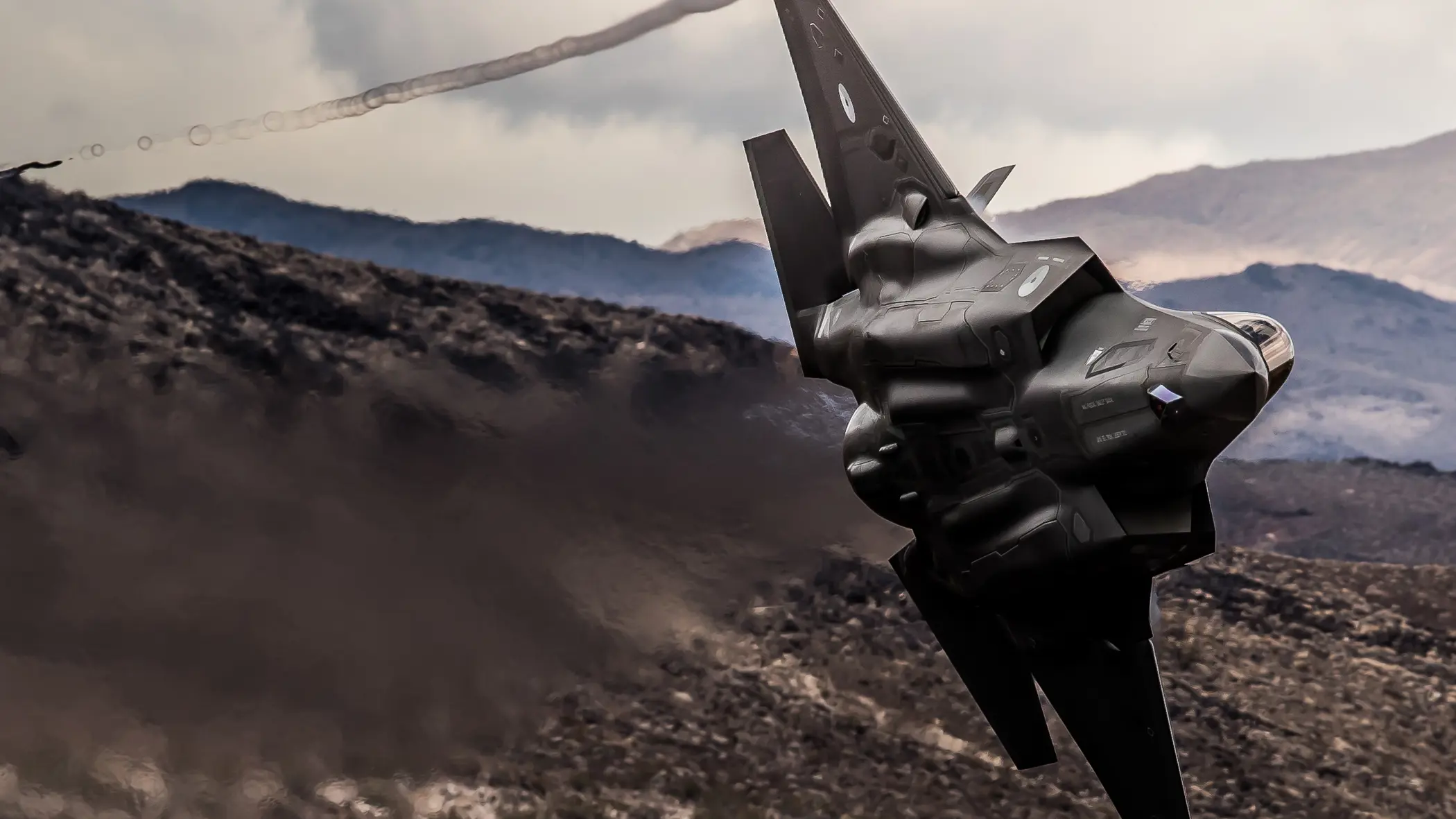 Een F-35 scheert door de lucht, op de achtergrond zijn bruine bergen te zien 