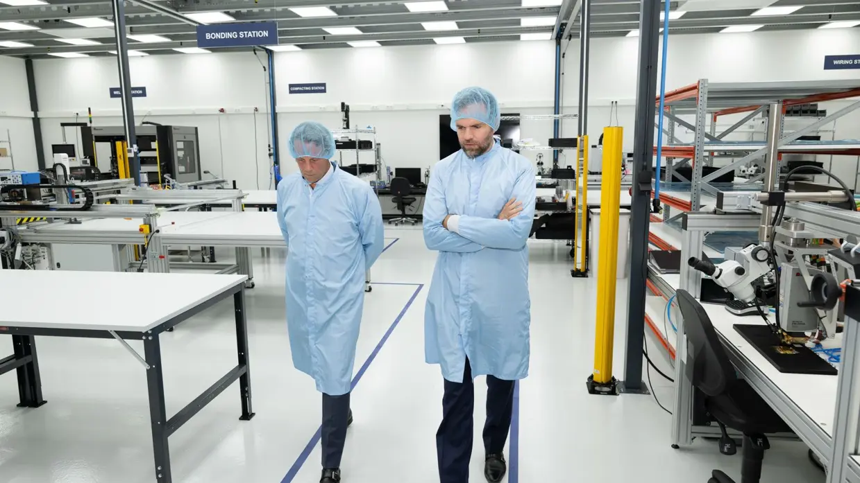 Twee mannen lopen in beschermende kleding door een fabriekshal.