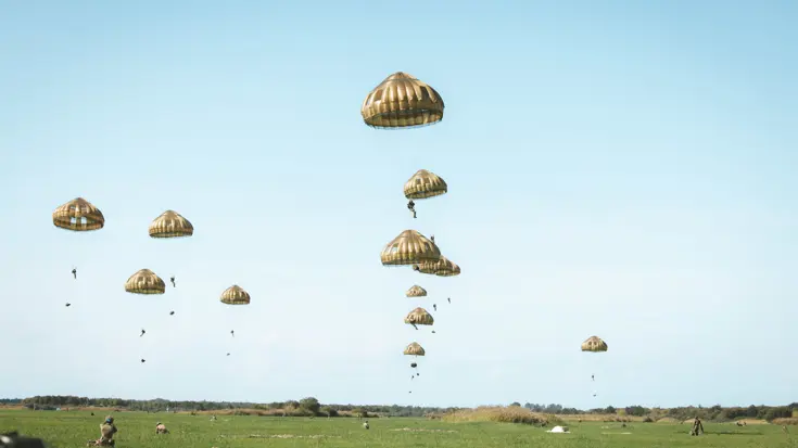 Parachutisten in de lucht boven grasveld.