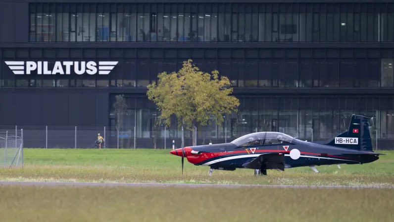 PC-7 MKX taxiet langs een donkergrijs gebouw waarop de naam Pilatus staat. 