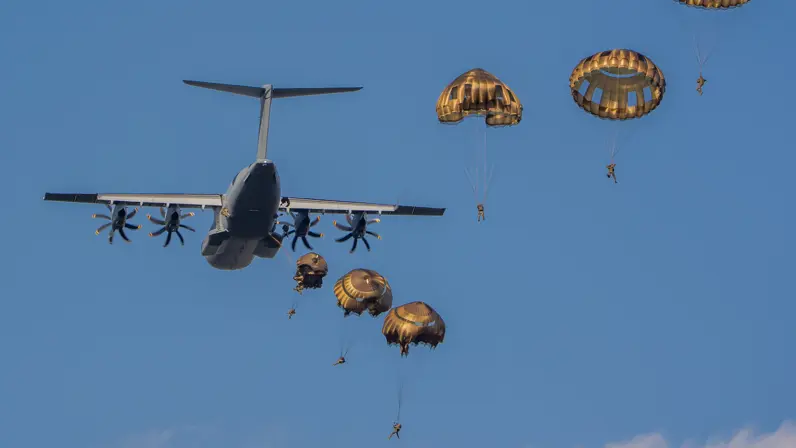 Een Duitse A400M dropt parachutisten tegen een blauwe lucht.