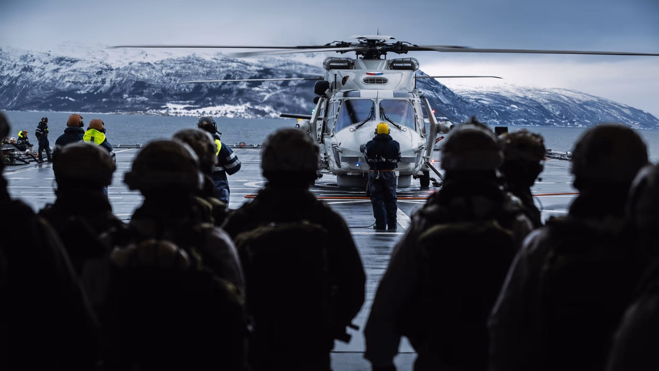 Mariniers, op de rug gezien, wachten op het helidek om in een NH90 te stappen.