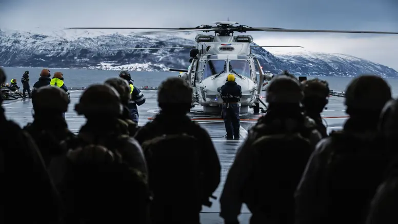 Mariniers, op de rug gezien, wachten op het helidek om in een NH90 te stappen.