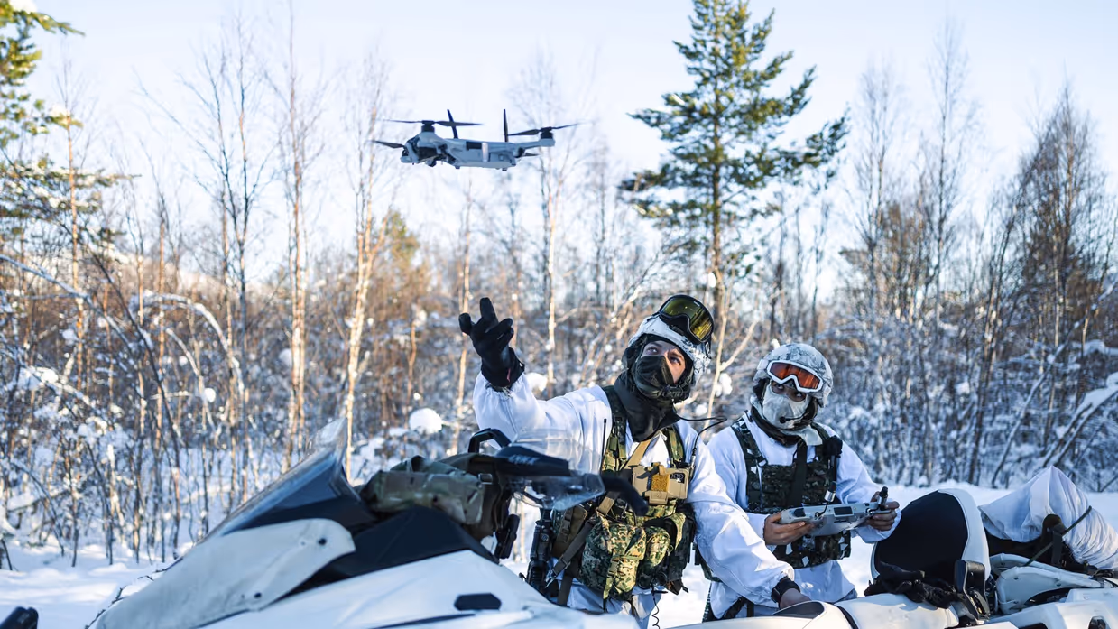 Twee mariniers gezeten op sneeuwscooters lanceren een drone.
