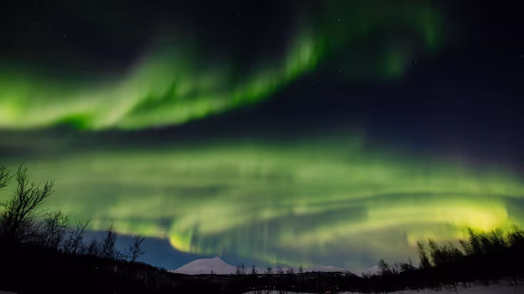Een sneeuwlandschap met daarboven het groene Noorderlicht. &nbsp;