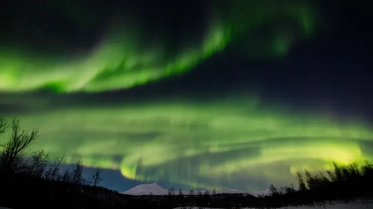 Een sneeuwlandschap met daarboven het groene Noorderlicht. &nbsp;