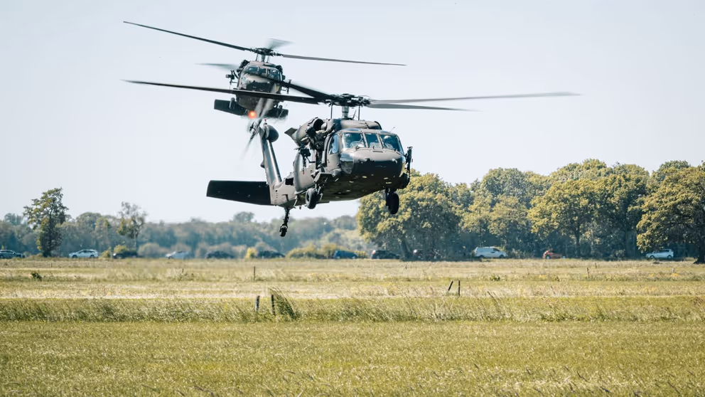 2 helikopters vliegen laag boven grasland.