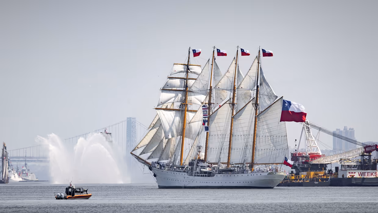 zijaanzicht van een groot wit zeilschip van de Amerikaanse Kustwacht met op de achtergrond de bebouwing van Manhattan.