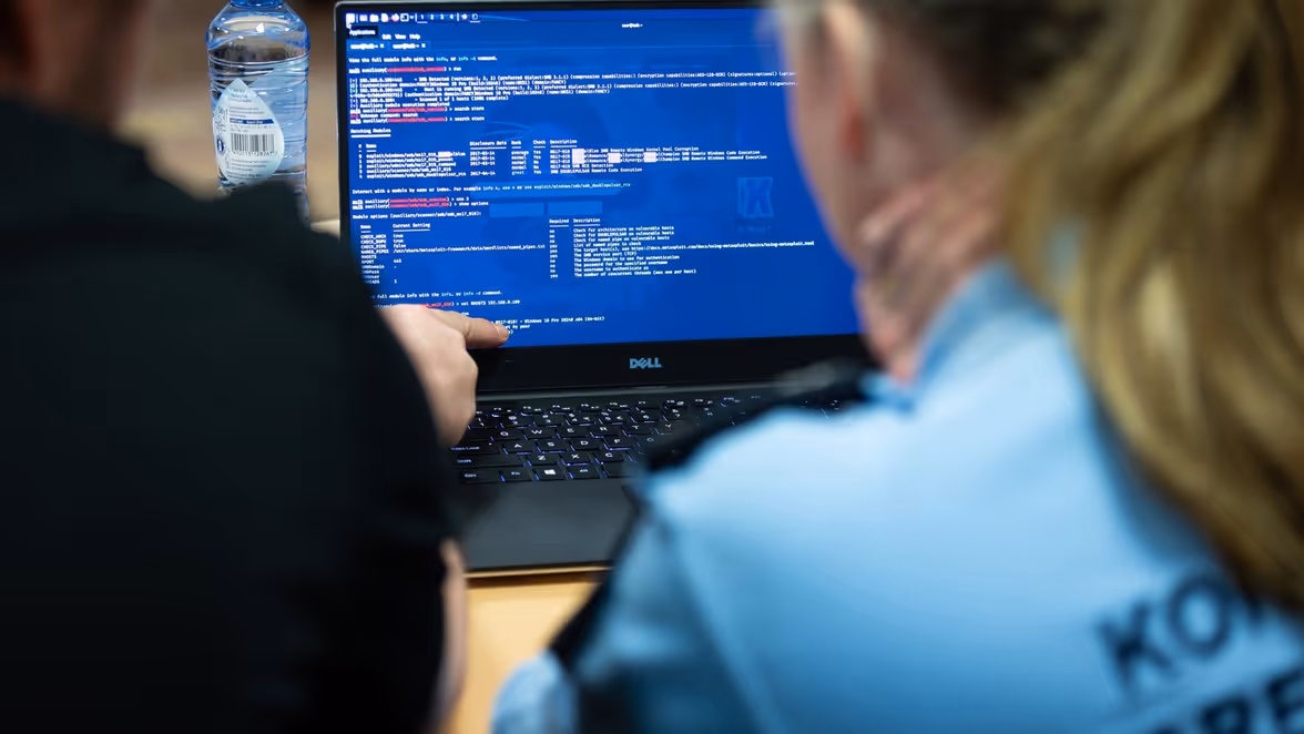 Een marechaussee op de rug gezien achter een computerscherm.