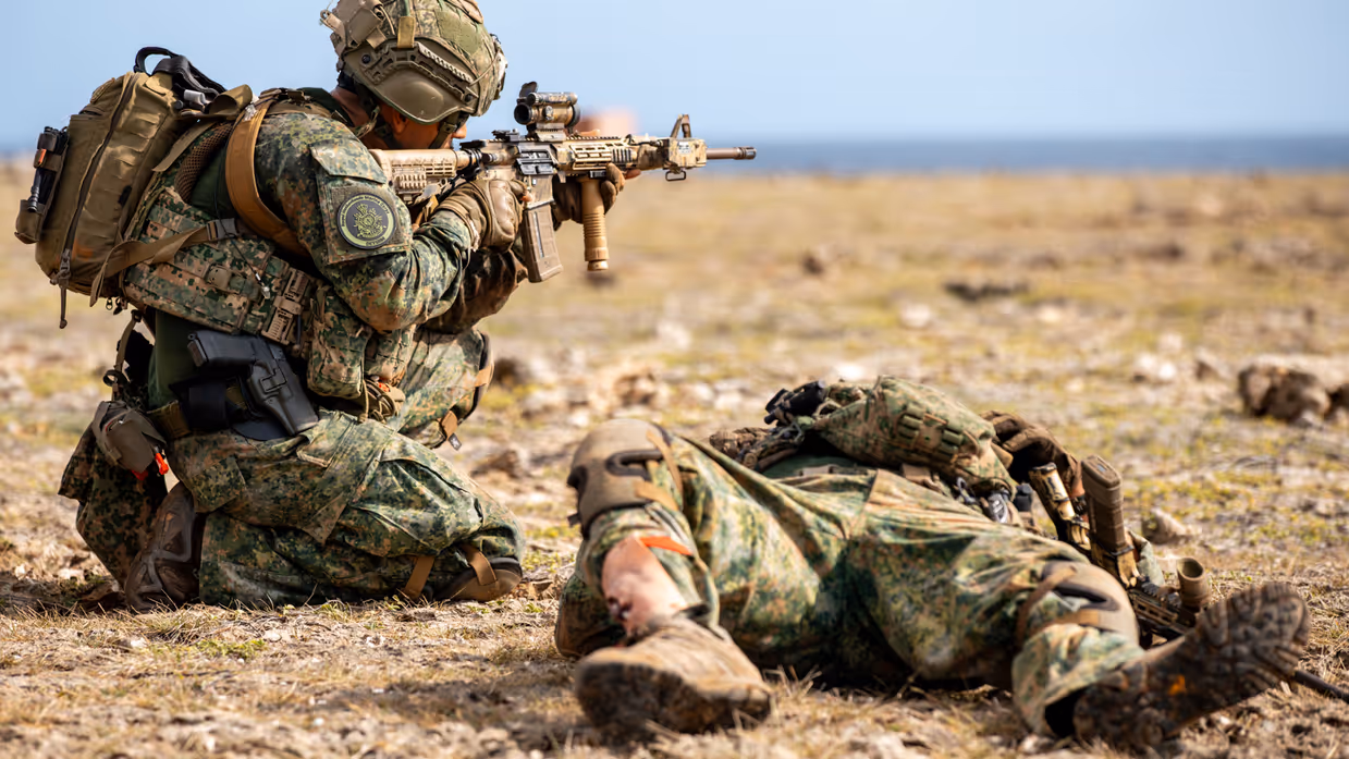 een militair vuurt knielend en naast hem ligt een zogenaamd gewonde militair. 