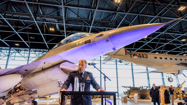 Tankink die zijn gehoor toespreekt met de J-063 op de achtergrond.