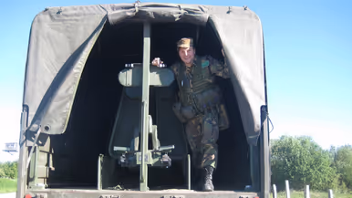 Een jonge Tim Nelissen in gevechtstenue poseert staand in de open achterkant van een militaire vrachtwagen en kijkt in de camera.