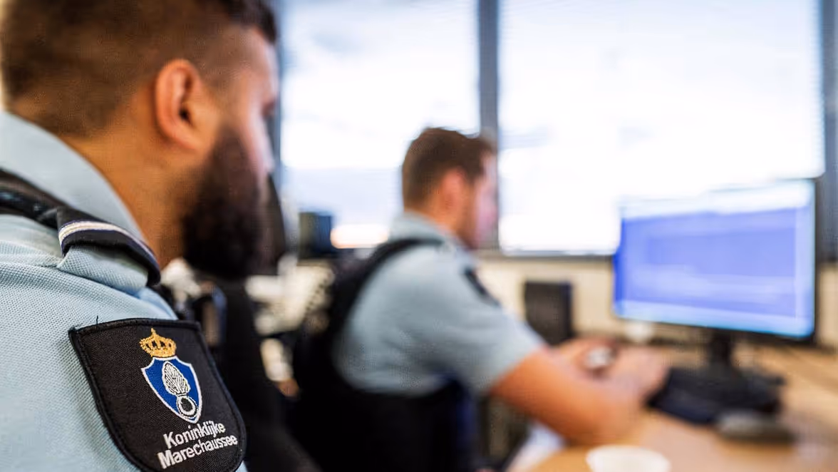 Twee marechaussees zitten achter een beeldscherm. 