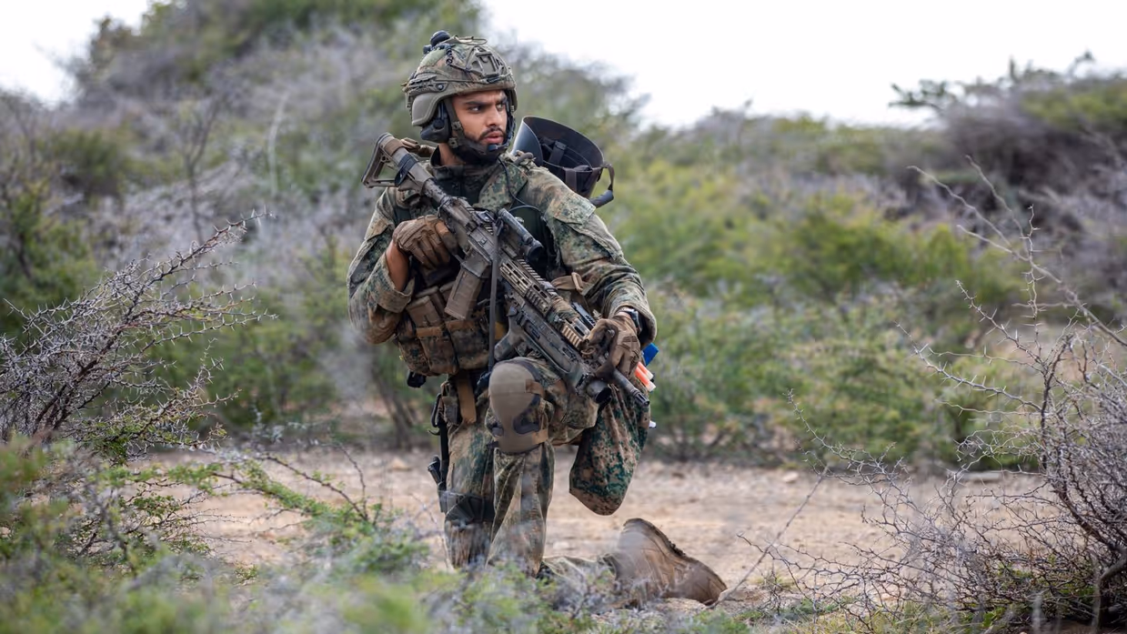 Een militair zit op een knie en tuurt in de verte. 