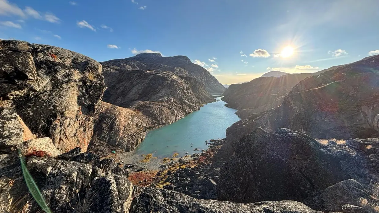  Een fjord met felgroen water en bruine rotsen en een strakke blauwe hemel. 