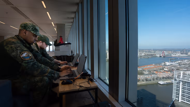  Twee militairen werken achter hun laptop. Het duo kijkt vanaf hun positie op hoogte uit op Rotterdam.