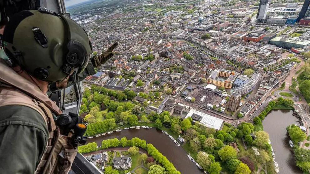 Gehelmde man kijkt vanuit een helikopter naar bebouwd gebied aan een rivier.