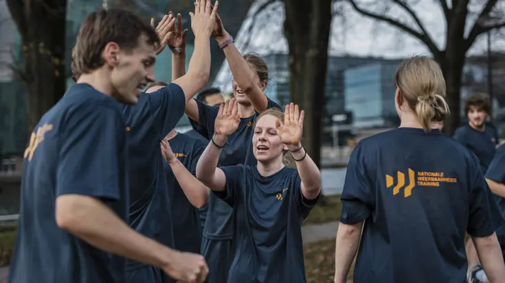 Jongeren geven elkaar high five. Op hun T-shirt staat de tekst Nationale Weerbaarheids Training. 