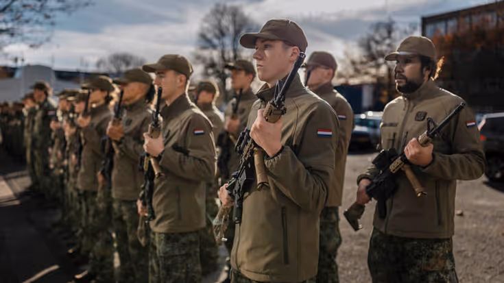2 rijen staande jonge reservisten met petjes op en een wapen op hun borst.