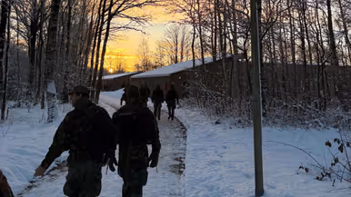 Deelnemers van de Nationale Weerbaarheidstraining lopen door een besneeuwd oefengebied tijdens zonsopkomst.