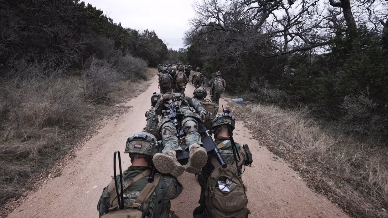 Militairen op een bospad dragen een gewonde militair op een brancard. 