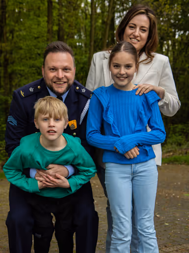 Tim poseert in zijn blauwe nette militaire pak tegen de bosrand samen met zijn vrouw, dochter en jongere zoon.