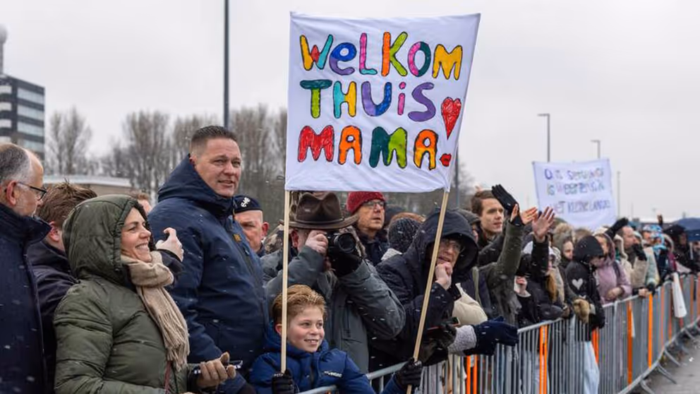 Mensen tonen een spandoek om militairen welkom terug te heten na inzet.