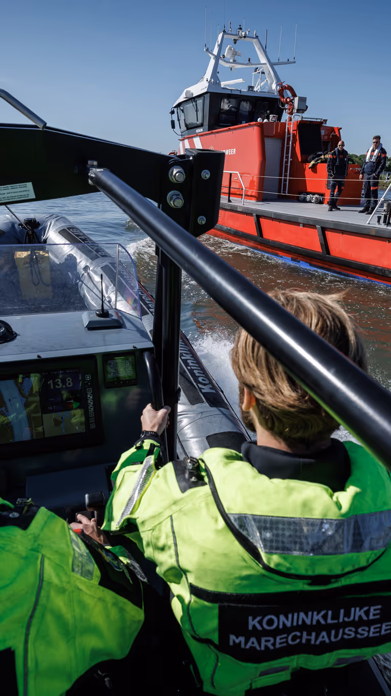 Marechaussees in een vaartuig met een boot van de brandweer op de achtergrond.
