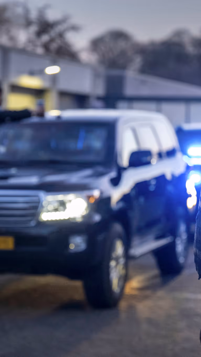 Een marechaussee staat bij een colonne dienstvoertuigen met ingeschakelde zwaailichten. 