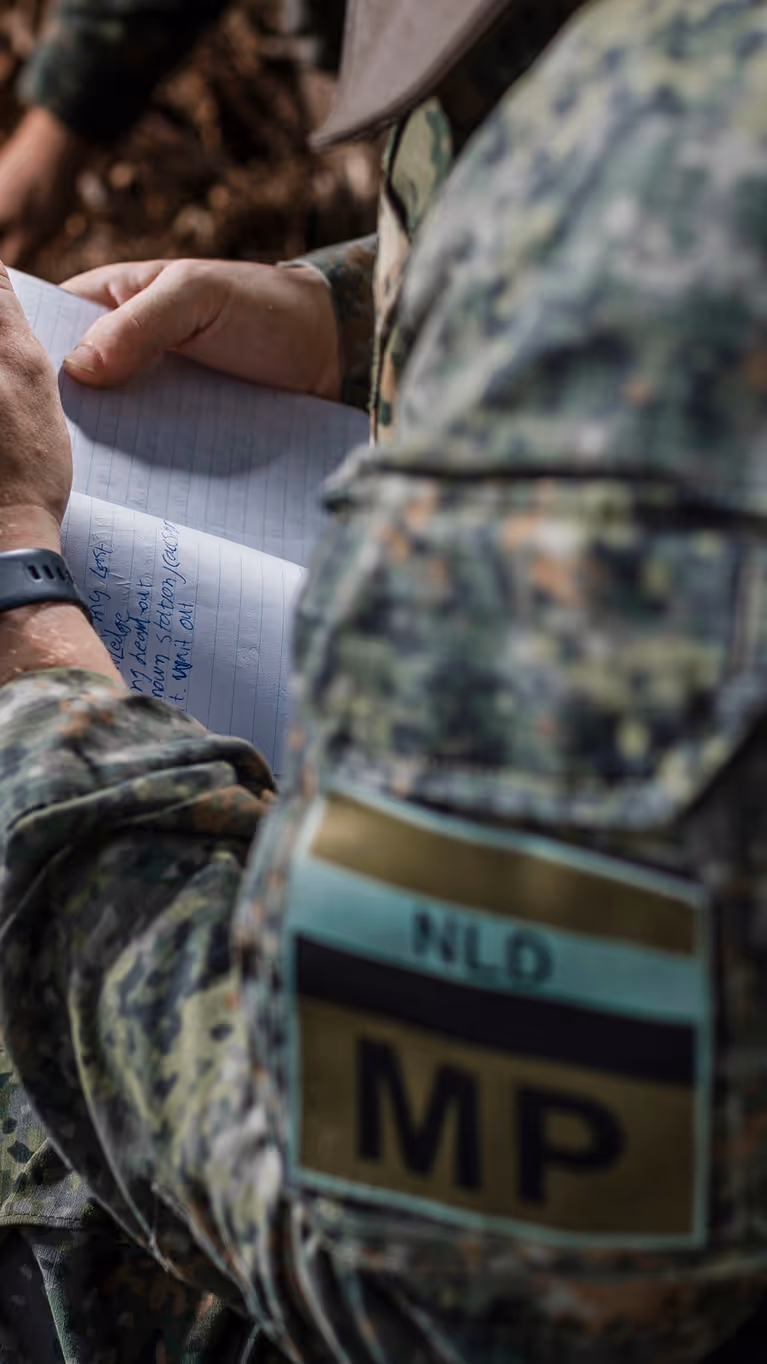 Een marechaussee van het MP-eskadron in groen tenue met een notitieblok en pen in zijn hand.