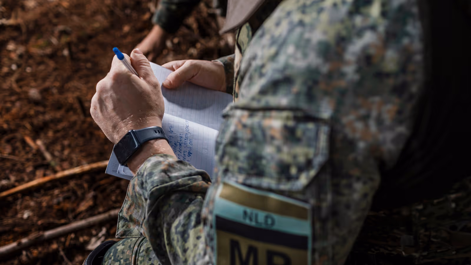 Een marechaussee van het MP-eskadron in groen tenue met een notitieblok en pen in zijn hand.