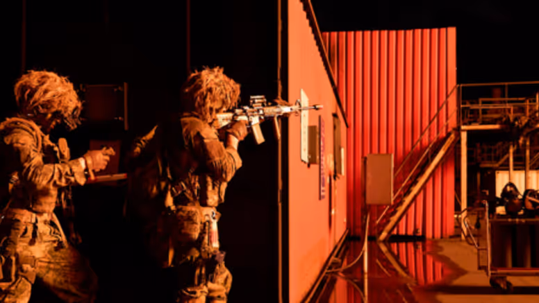 Mariniers bewegen zich langs een container bij nacht en richten hun wapens.