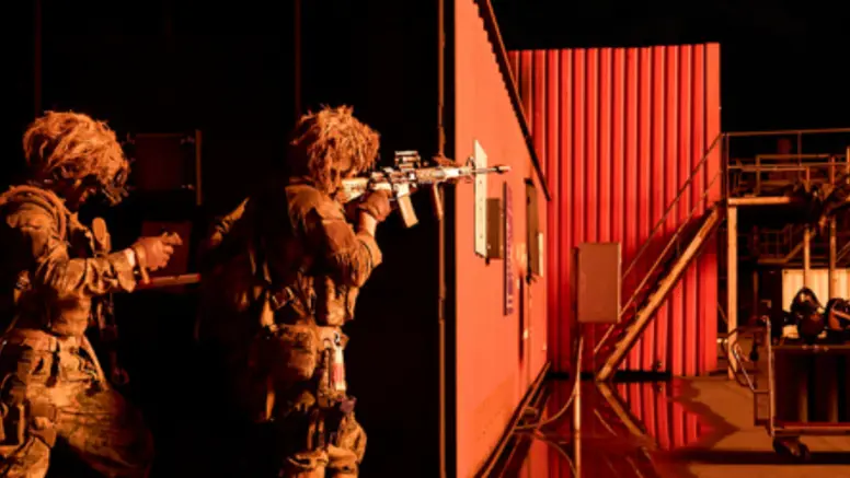Mariniers bewegen zich langs een container bij nacht en richten hun wapens.