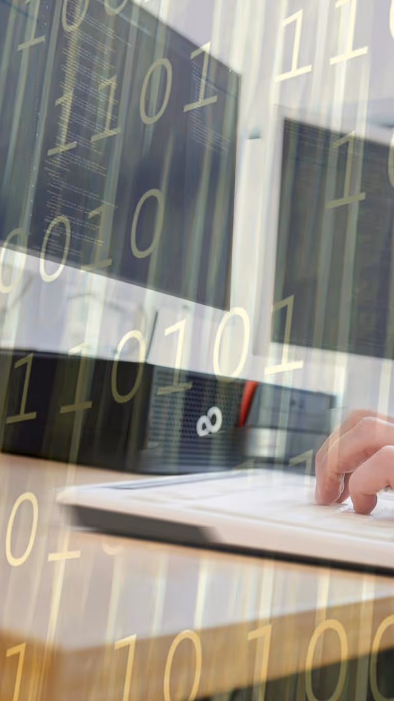 Een paar handen op een toetsenbord, achter computerschermen.