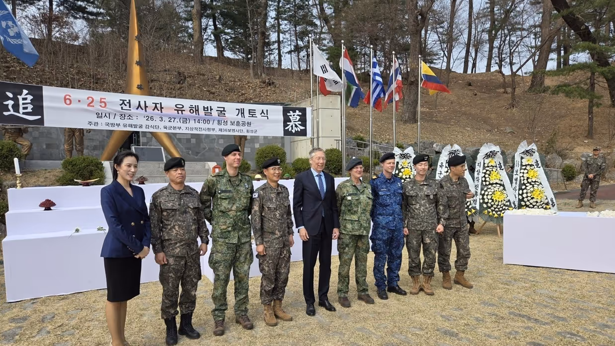 Een groep militairen staat opgesteld. Met Leon Diender met tenue 6 in het midden. Achter hen is een banier te zien met Koreaanse tekens.