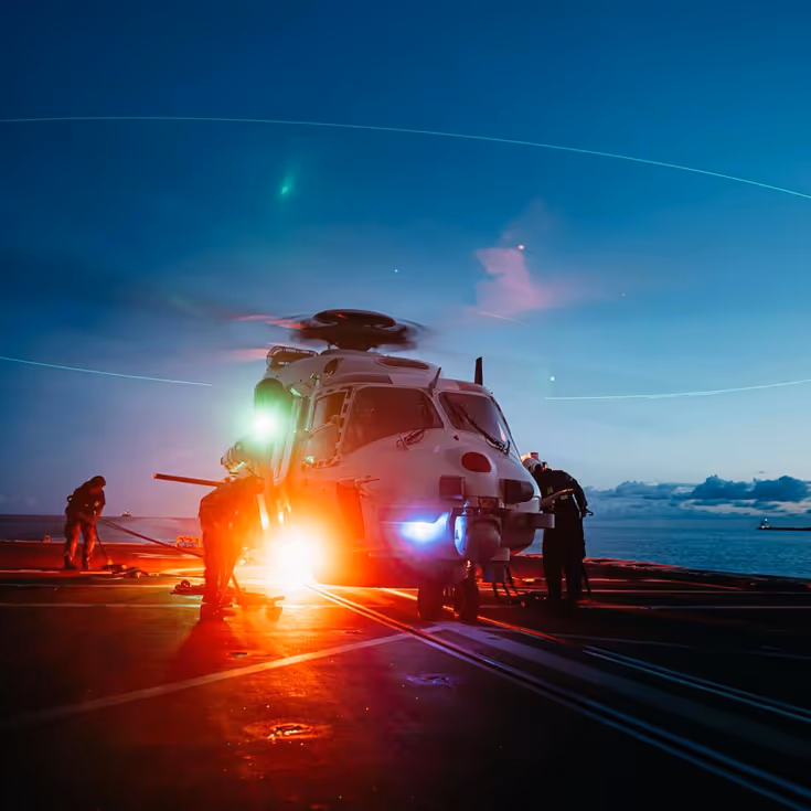 Een NH90 staat met draaiende rotorbladen bij invallende duisternis op het helidek.