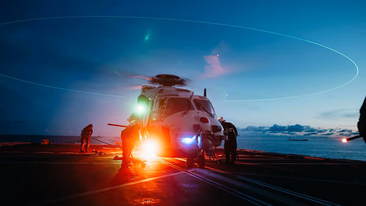 Een NH90 staat met draaiende rotorbladen bij invallende duisternis op het helidek.