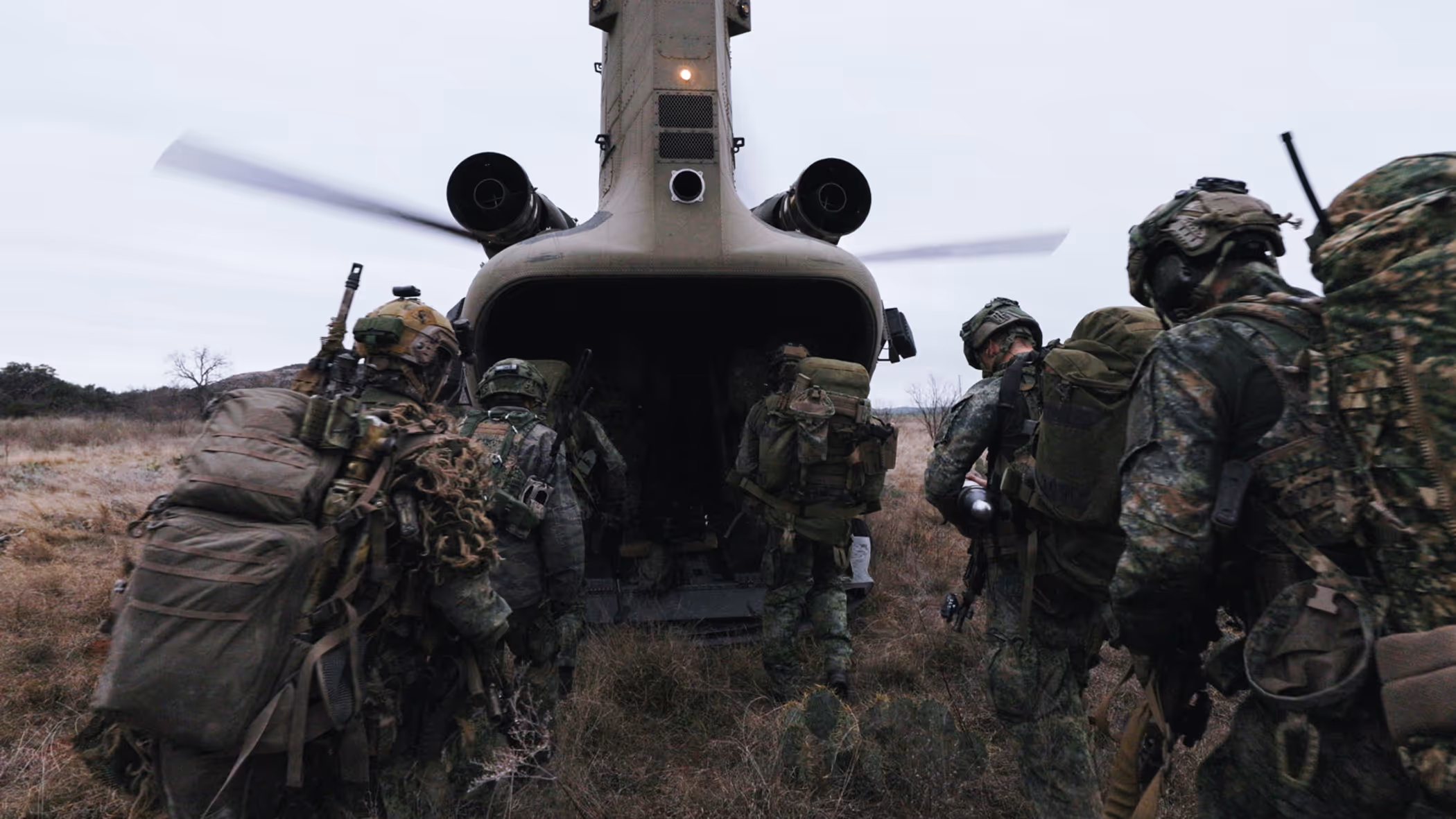 Militairen in het veld lopen via de laadklep een Chinook met draaiende rotors in.